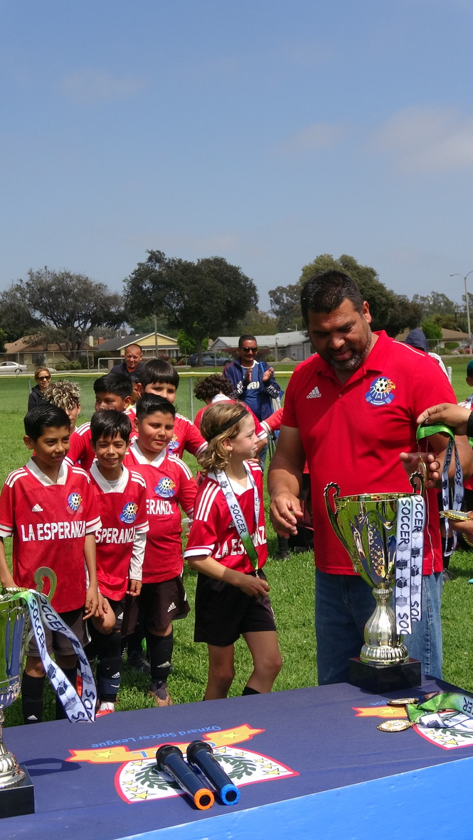 Young La Esperanza players and coach celebrating with a trophy