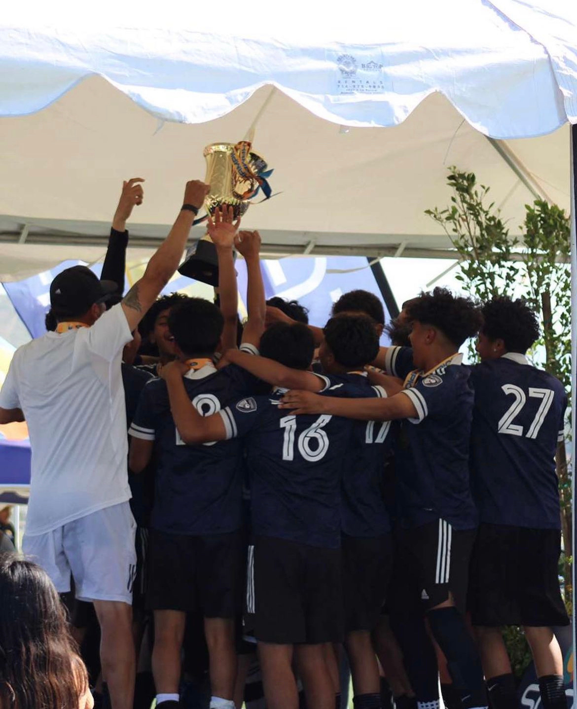 La Esperanza players lifting a trophy under a tournament tent